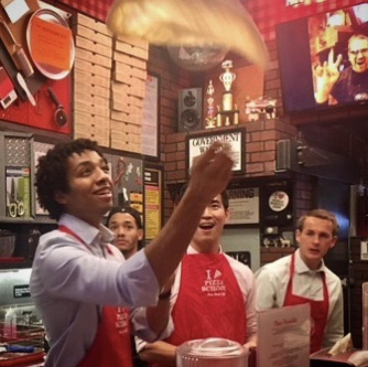 Men tossing dough at a pizza making class